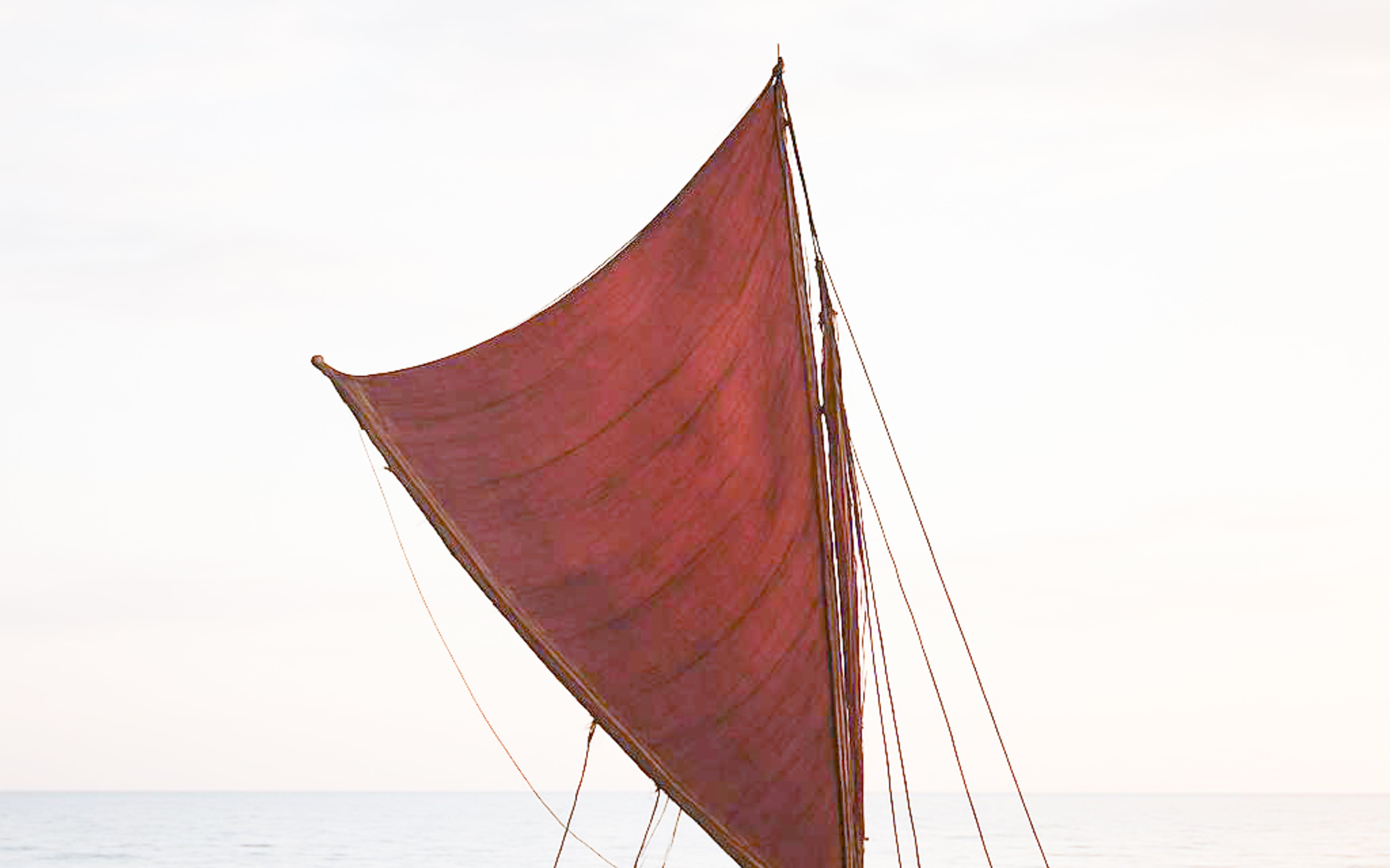 Traditional wooden sailboat with a red sail on calm waters