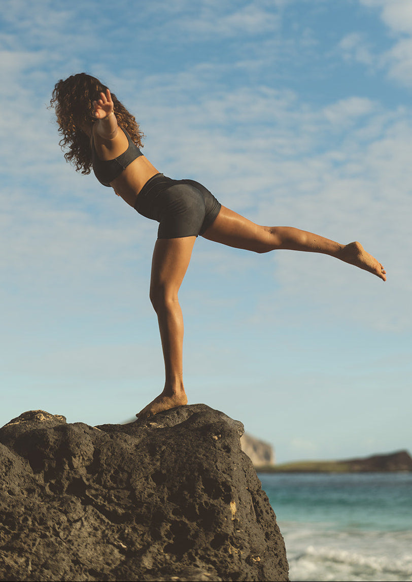 Person practicing yoga on a rock with a blue sky and ocean background